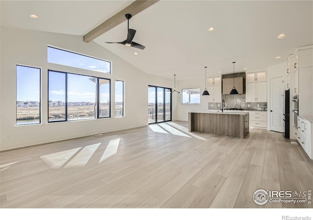 kitchen with white cabinetry, decorative backsplash, a large island with sink, and pendant lighting