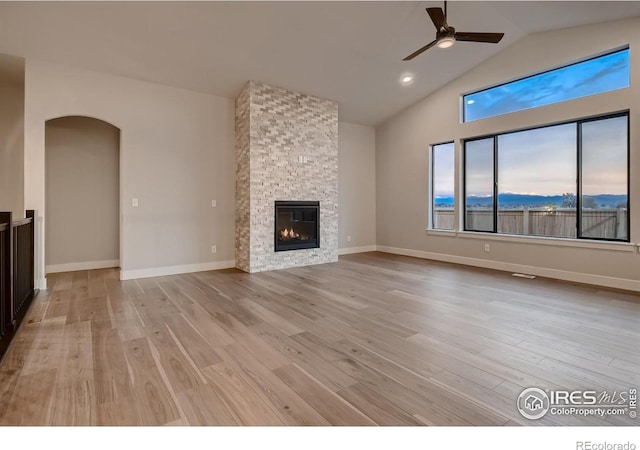 unfurnished living room with light wood-type flooring, ceiling fan, lofted ceiling, and a stone fireplace