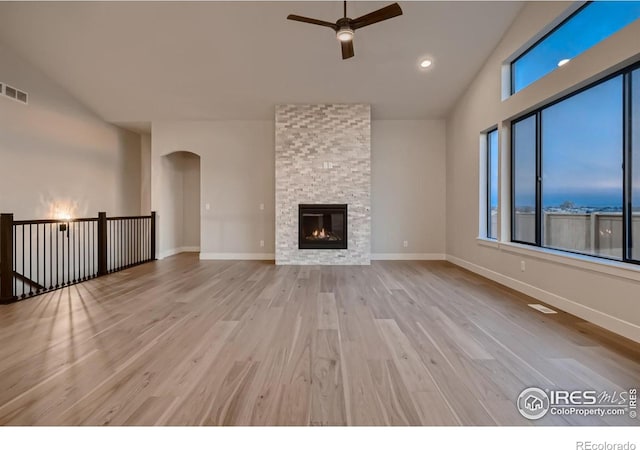 unfurnished living room featuring ceiling fan, vaulted ceiling, a stone fireplace, and light wood-type flooring