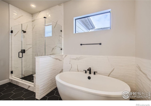 bathroom with tile walls, separate shower and tub, and tile patterned flooring