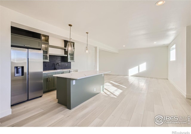 kitchen featuring backsplash, pendant lighting, sink, light stone countertops, and stainless steel fridge