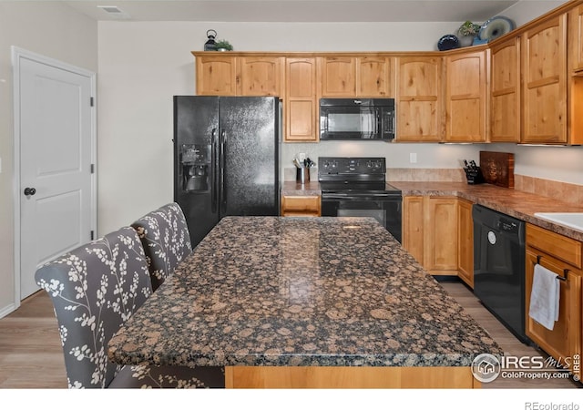 kitchen featuring a center island, dark stone counters, light hardwood / wood-style floors, and black appliances