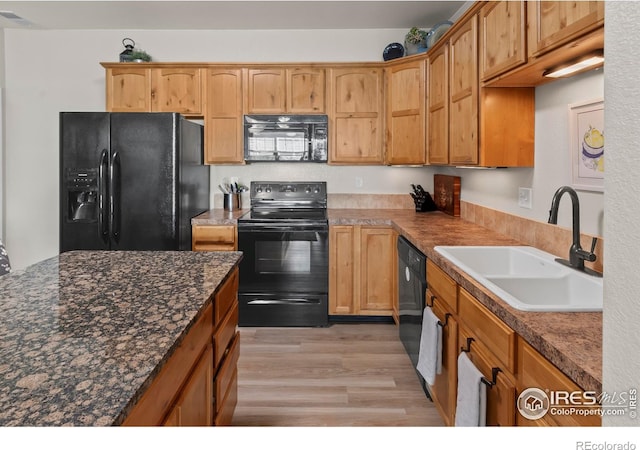 kitchen featuring dark stone countertops, sink, light hardwood / wood-style flooring, and black appliances