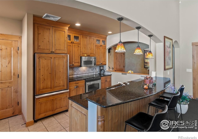 kitchen featuring sink, a breakfast bar, appliances with stainless steel finishes, dark stone countertops, and hanging light fixtures