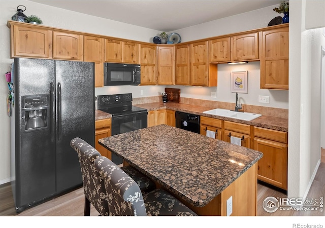 kitchen featuring a kitchen island, sink, dark stone countertops, a kitchen breakfast bar, and black appliances