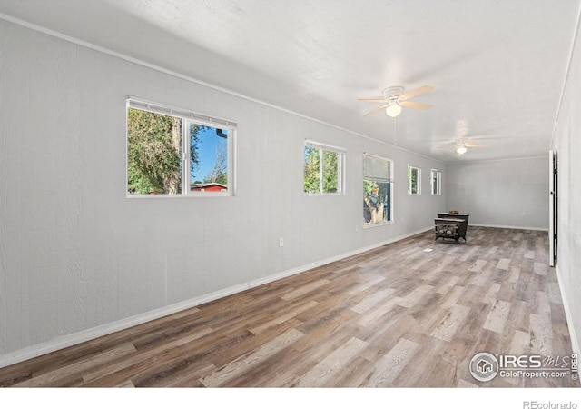 unfurnished room featuring ceiling fan, light wood-type flooring, crown molding, and a wood stove