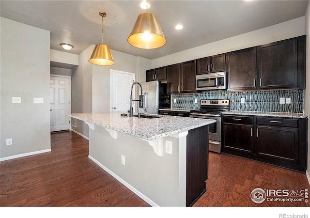 kitchen featuring an island with sink, sink, stainless steel appliances, light stone countertops, and dark hardwood / wood-style flooring