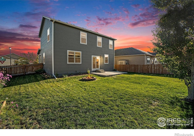 back house at dusk with a lawn and a patio area