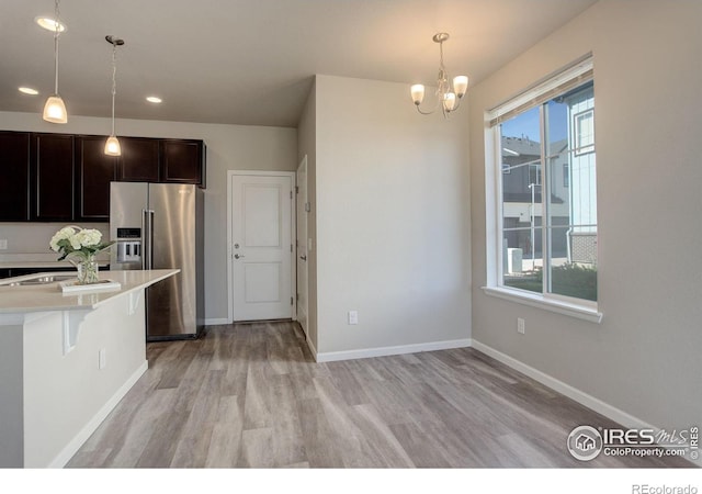 kitchen with high end refrigerator, hanging light fixtures, a breakfast bar, dark brown cabinetry, and light wood-type flooring