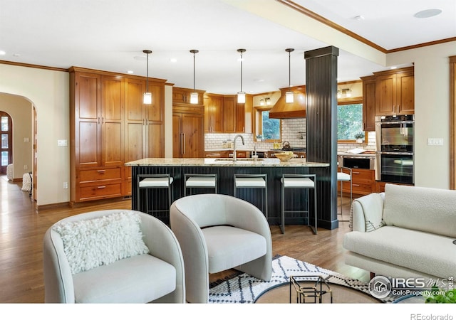 kitchen with stainless steel double oven, paneled refrigerator, hanging light fixtures, and light wood-type flooring