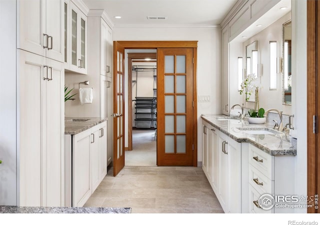 kitchen with white cabinetry, light stone countertops, and sink