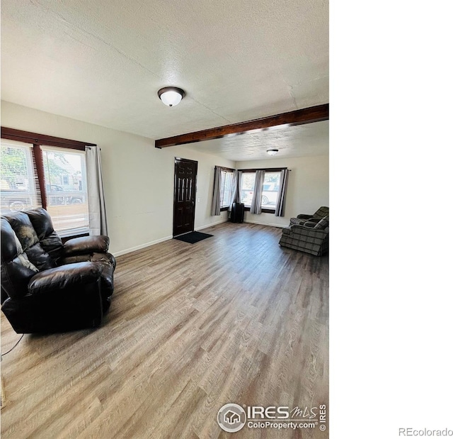 living room featuring beamed ceiling, a textured ceiling, and light wood-type flooring