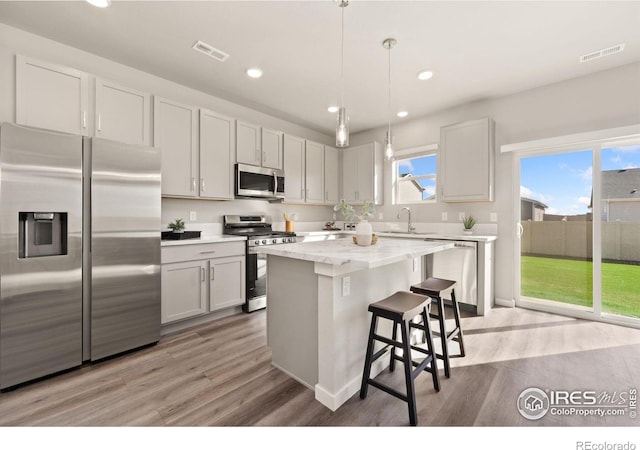 kitchen featuring pendant lighting, stainless steel appliances, a center island, light hardwood / wood-style floors, and light stone countertops