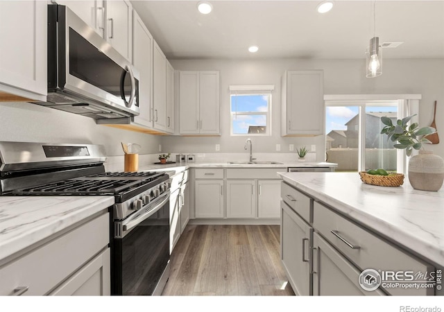 kitchen with white cabinetry, sink, light stone counters, stainless steel appliances, and light hardwood / wood-style flooring