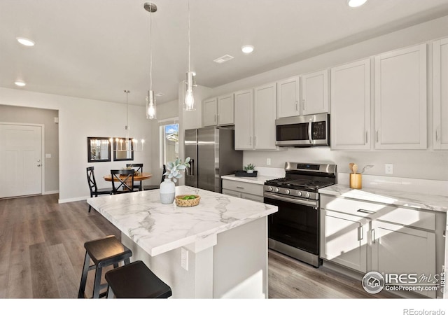 kitchen with pendant lighting, stainless steel appliances, light stone counters, white cabinets, and a kitchen island