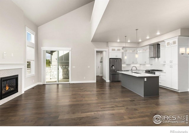 kitchen with a kitchen island with sink, wall chimney exhaust hood, hanging light fixtures, stainless steel appliances, and dark hardwood / wood-style flooring