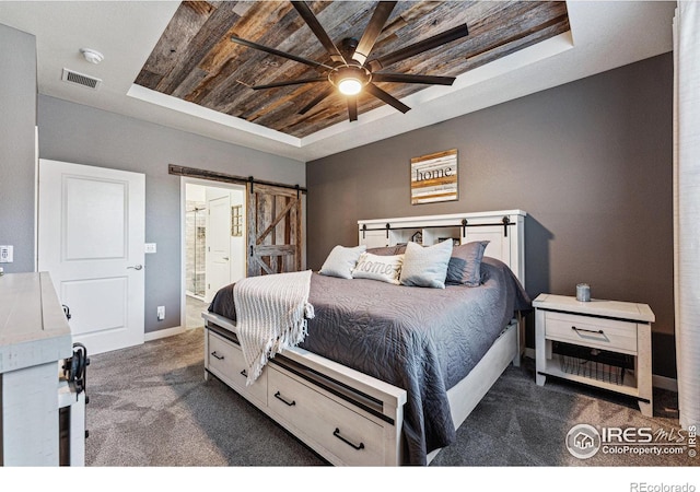 carpeted bedroom with a raised ceiling, a barn door, ensuite bathroom, and ceiling fan