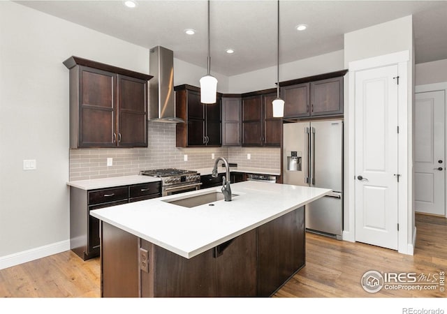 kitchen featuring wall chimney range hood, hanging light fixtures, light hardwood / wood-style flooring, sink, and high end appliances