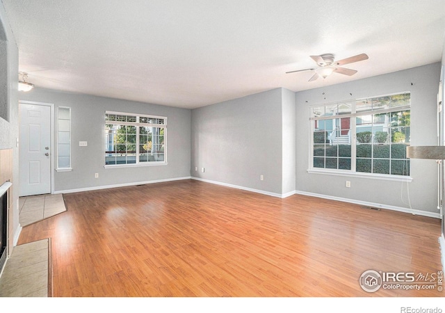 unfurnished living room featuring ceiling fan, a tile fireplace, a textured ceiling, and wood-type flooring