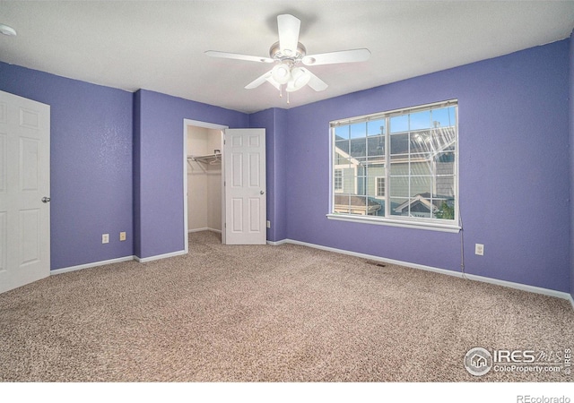 unfurnished bedroom featuring a closet, ceiling fan, carpet, and a spacious closet