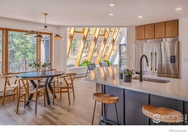 kitchen featuring stainless steel fridge, a kitchen bar, light wood-type flooring, pendant lighting, and sink