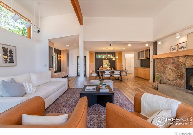 living room with light hardwood / wood-style floors, a stone fireplace, a towering ceiling, and beam ceiling