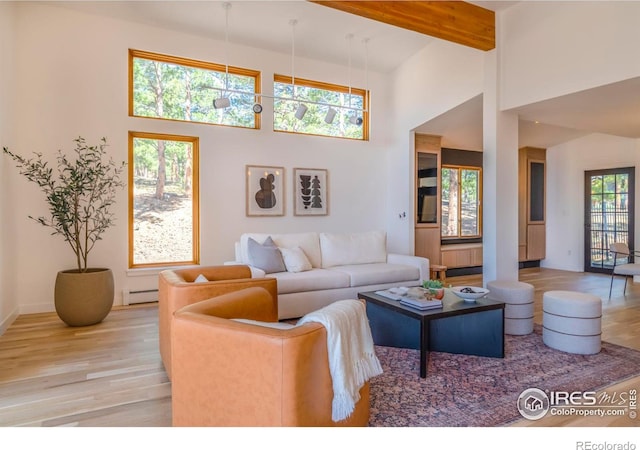 living room with a towering ceiling, baseboard heating, beam ceiling, and light wood-type flooring