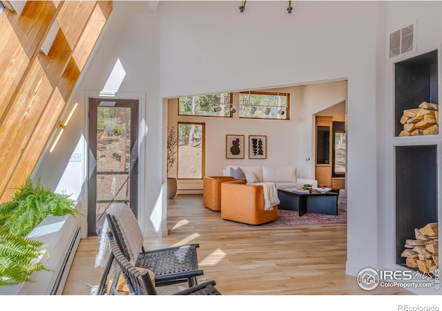 living room featuring a high ceiling, a baseboard heating unit, light wood-type flooring, and a skylight