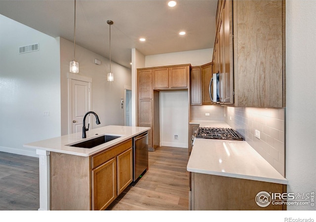 kitchen with sink, stainless steel appliances, pendant lighting, light hardwood / wood-style flooring, and a kitchen island with sink