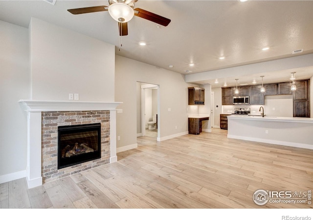 unfurnished living room with light hardwood / wood-style flooring, sink, a fireplace, and ceiling fan