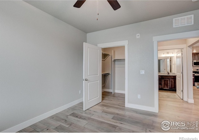 unfurnished bedroom featuring a closet, a walk in closet, light hardwood / wood-style floors, and ceiling fan