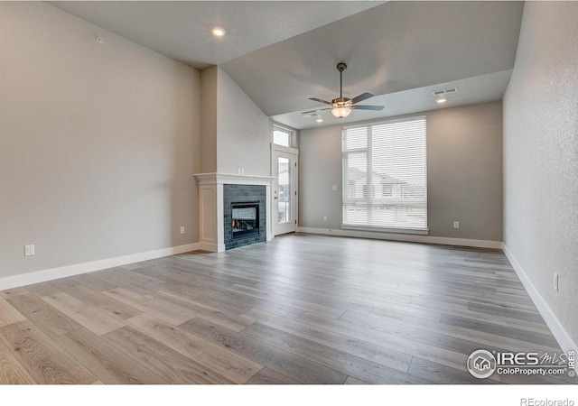 unfurnished living room with light hardwood / wood-style flooring, a tiled fireplace, high vaulted ceiling, and ceiling fan