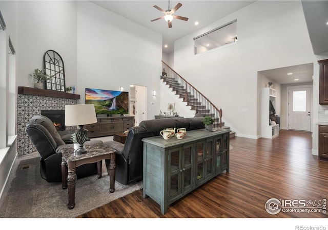 living room featuring a tile fireplace, dark wood-type flooring, a high ceiling, and ceiling fan