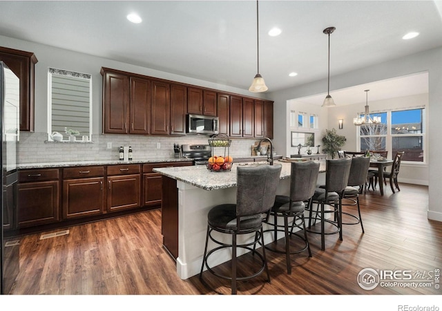 kitchen featuring appliances with stainless steel finishes, dark hardwood / wood-style flooring, a center island with sink, and hanging light fixtures