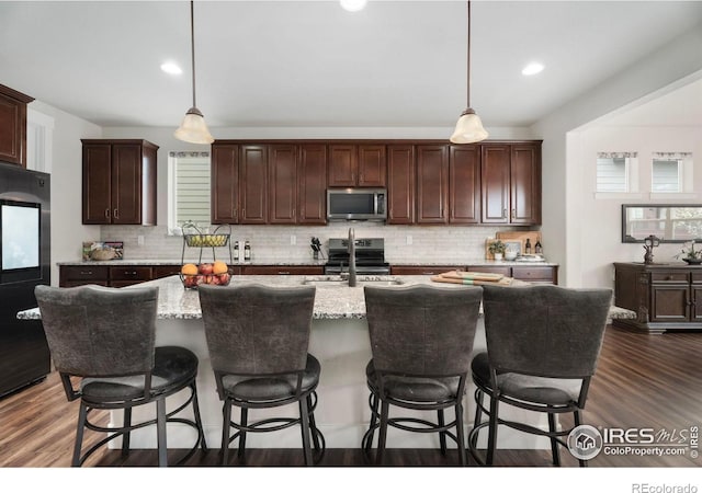 kitchen featuring stainless steel appliances, decorative light fixtures, a center island with sink, and dark hardwood / wood-style flooring