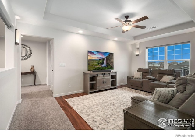 living room with ceiling fan, a tray ceiling, and dark hardwood / wood-style flooring