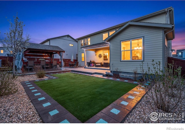 back house at dusk with a gazebo, a patio area, and a yard