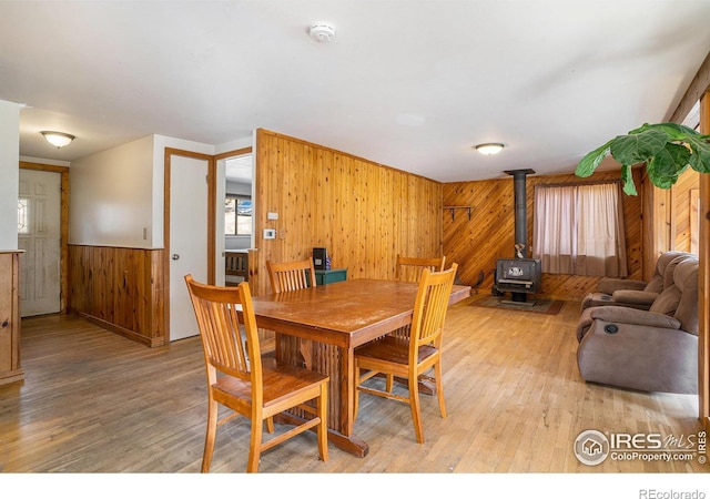 dining space featuring a wood stove, wood walls, and light hardwood / wood-style flooring