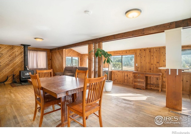 dining area with a wood stove, beamed ceiling, and light hardwood / wood-style flooring