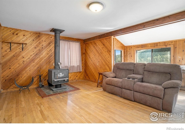 living room with a wood stove, lofted ceiling with beams, wood walls, and wood-type flooring