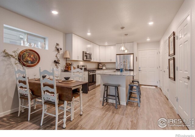 kitchen with a kitchen breakfast bar, stainless steel appliances, a center island with sink, decorative light fixtures, and white cabinetry