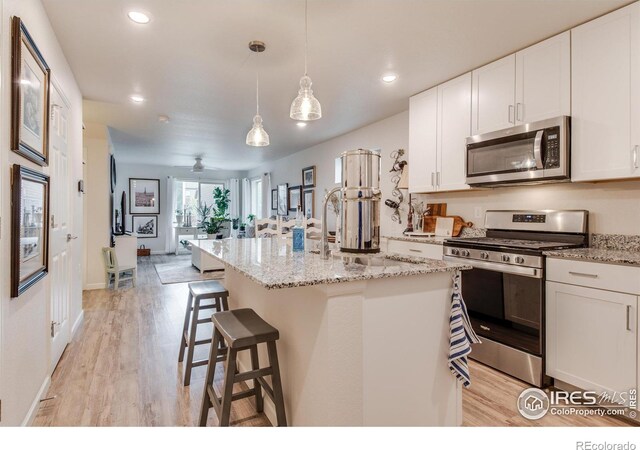 kitchen with white cabinetry, a kitchen island with sink, light hardwood / wood-style floors, decorative light fixtures, and stainless steel appliances