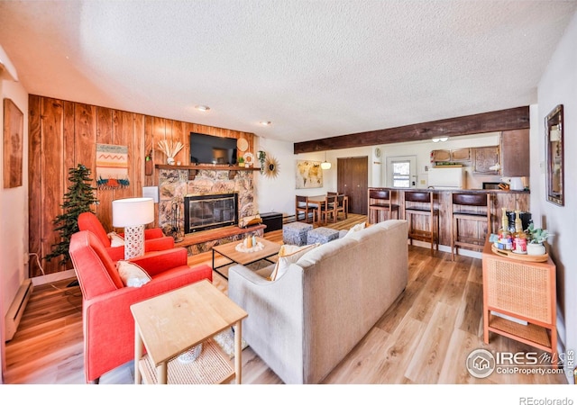 living room with a textured ceiling, light wood-type flooring, wood walls, a fireplace, and baseboard heating