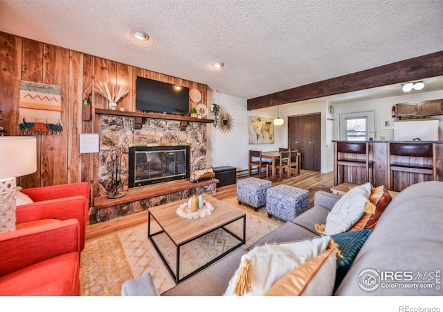 living room with beamed ceiling, a textured ceiling, a stone fireplace, and wood-type flooring