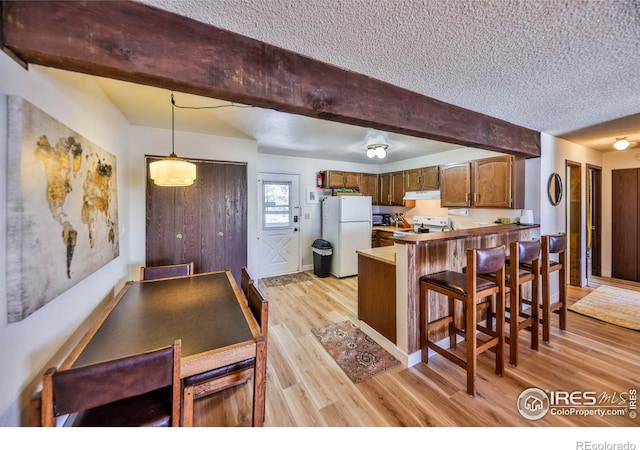 kitchen with a kitchen bar, kitchen peninsula, hanging light fixtures, white fridge, and light hardwood / wood-style flooring