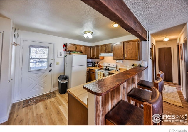 kitchen featuring white appliances, a kitchen bar, light hardwood / wood-style flooring, and kitchen peninsula