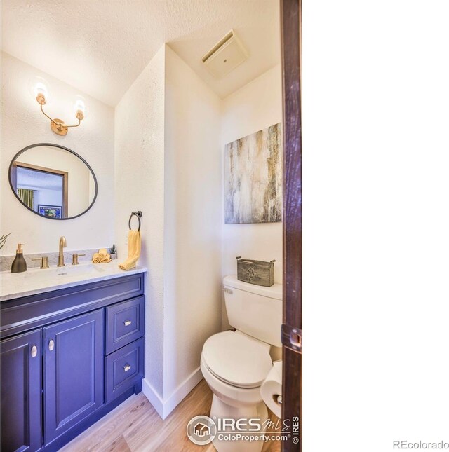 bathroom with hardwood / wood-style floors, a textured ceiling, vaulted ceiling, toilet, and vanity