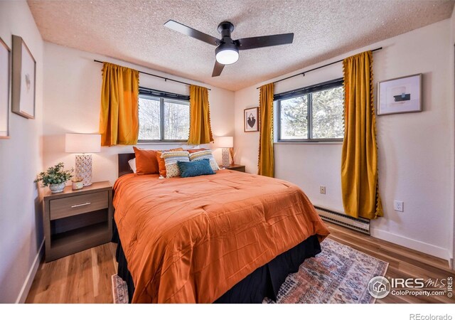 bedroom with a baseboard radiator, multiple windows, wood-type flooring, and ceiling fan