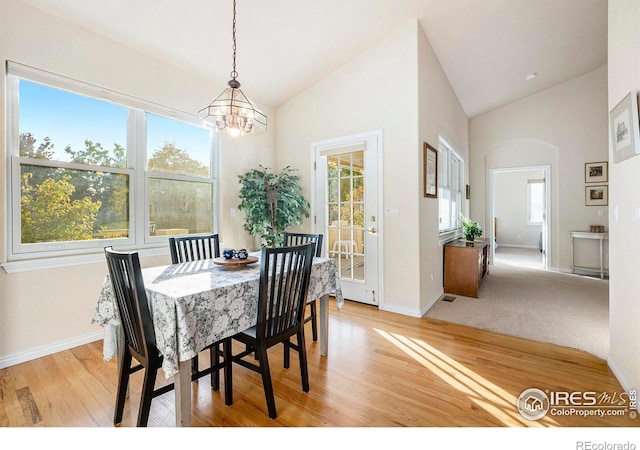 dining room featuring lofted ceiling, light hardwood / wood-style floors, a notable chandelier, and a healthy amount of sunlight