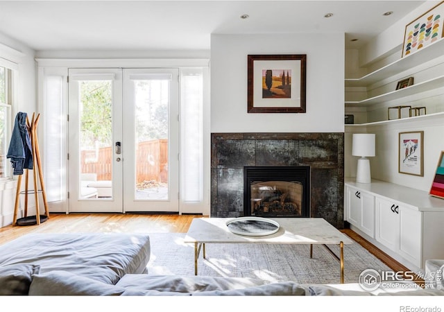 living room featuring french doors, a tiled fireplace, and light hardwood / wood-style flooring